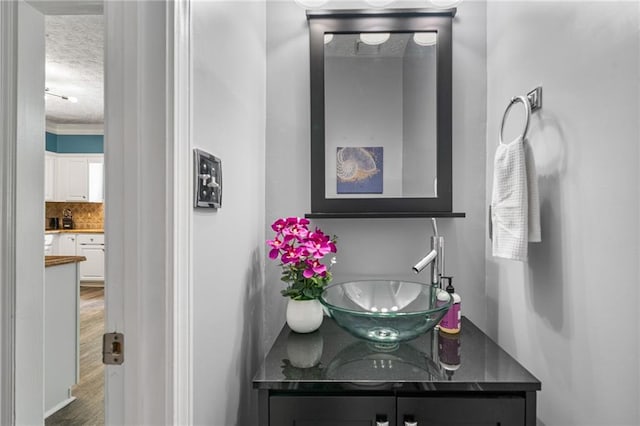 340 Chandler Ct, Sugar Hill, GA 30518 - bathroom featuring vanity, a textured ceiling, decorative backsplash, wood finished floors, and crown molding