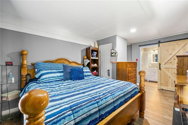 bedroom with hardwood / wood-style floors, ensuite bathroom, and a barn door