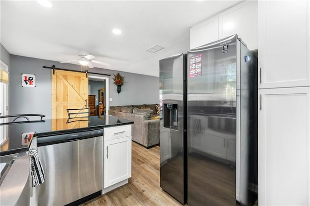 kitchen with white cabinets, light hardwood / wood-style floors, a barn door, and appliances with stainless steel finishes