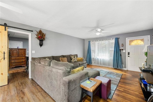 living room featuring wood-type flooring, ceiling fan, and a barn door