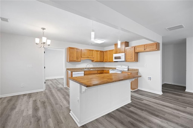 kitchen featuring white appliances, wood-type flooring, butcher block counters, sink, and hanging light fixtures