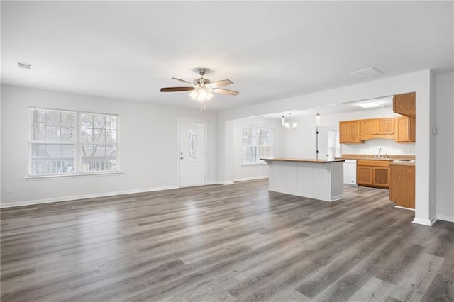 unfurnished living room with sink, ceiling fan with notable chandelier, and dark hardwood / wood-style floors