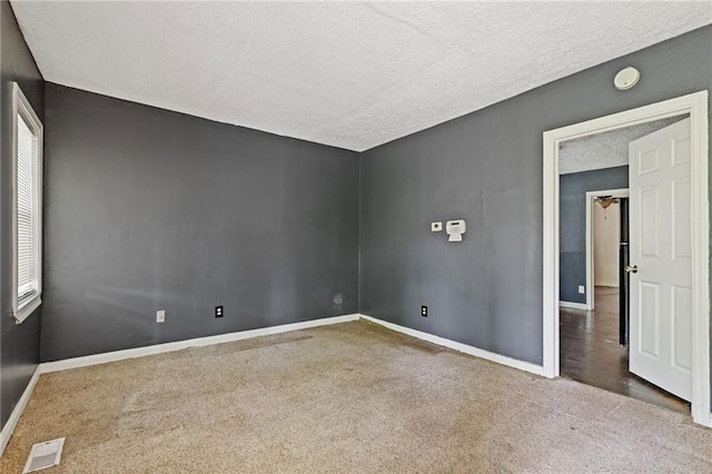 carpeted spare room featuring a textured ceiling, visible vents, and baseboards