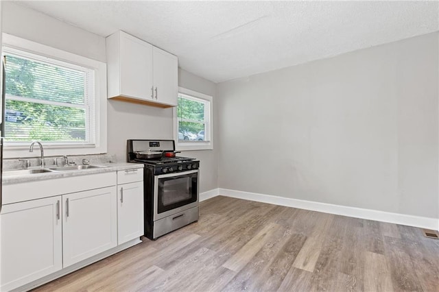 kitchen with light wood finished floors, light countertops, white cabinetry, a sink, and gas stove