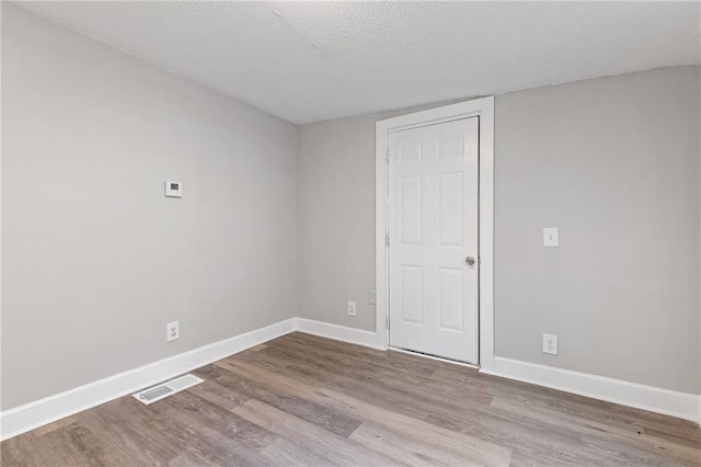 spare room featuring visible vents, a textured ceiling, baseboards, and wood finished floors