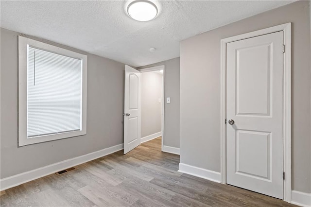 unfurnished bedroom featuring a textured ceiling, wood finished floors, visible vents, and baseboards