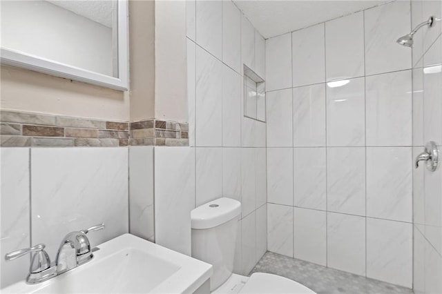 full bathroom featuring toilet, tile walls, a sink, and tiled shower