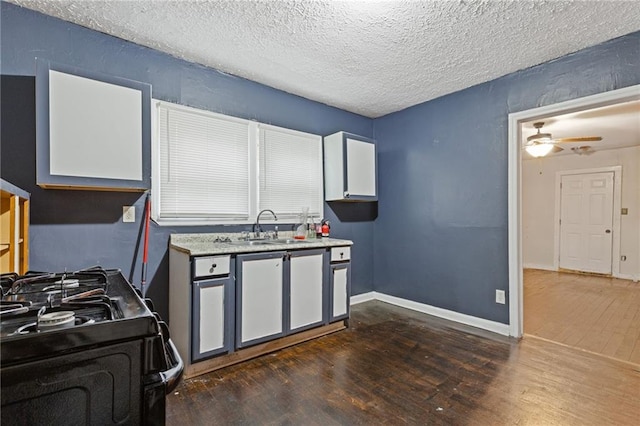 kitchen with a sink, black gas stove, baseboards, light countertops, and dark wood finished floors