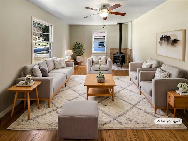 living room featuring ceiling fan, baseboards, wood finished floors, and a wood stove