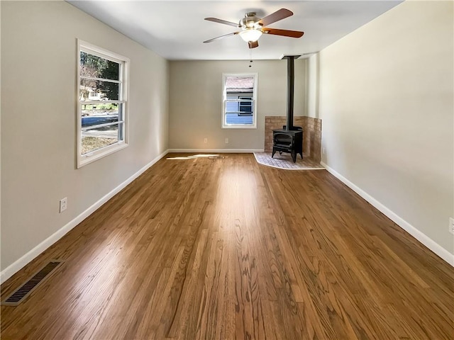 unfurnished living room with a wood stove, wood finished floors, visible vents, and baseboards