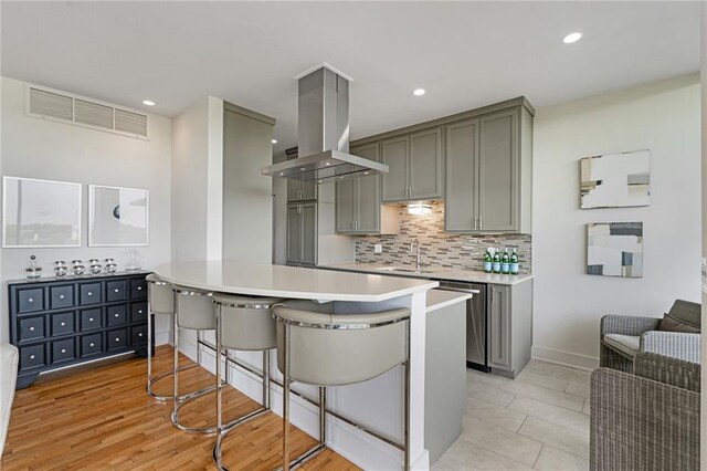 kitchen with gray cabinets, a breakfast bar area, island range hood, and decorative backsplash