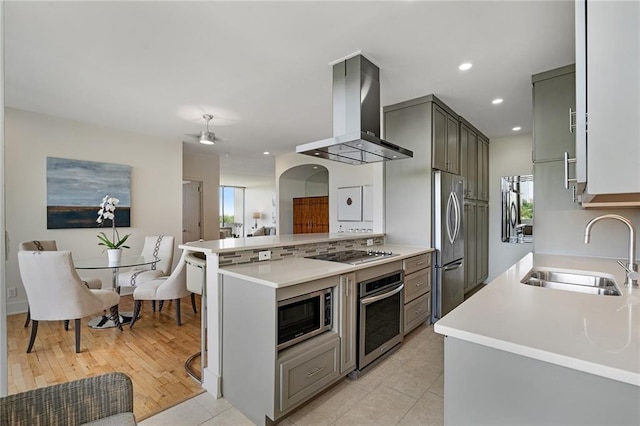 kitchen featuring kitchen peninsula, gray cabinetry, sink, appliances with stainless steel finishes, and island range hood