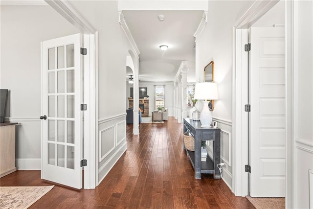 hall with arched walkways, dark wood-style flooring, ornamental molding, wainscoting, and a decorative wall