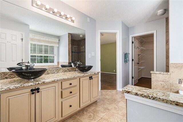 6411 Compass Dr, Flowery Branch, GA 30542 - bathroom featuring a stall shower, double vanity, a spacious closet, a textured ceiling, and tile patterned flooring
