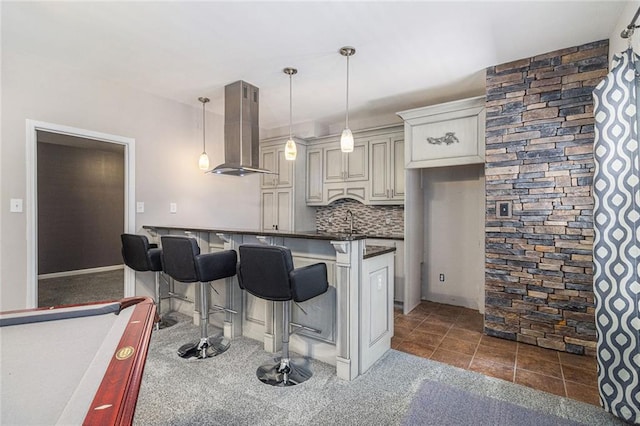 6411 Compass Dr, Flowery Branch, GA 30542 - kitchen with wall chimney exhaust hood, dark countertops, a kitchen bar, tasteful backsplash, and hanging light fixtures