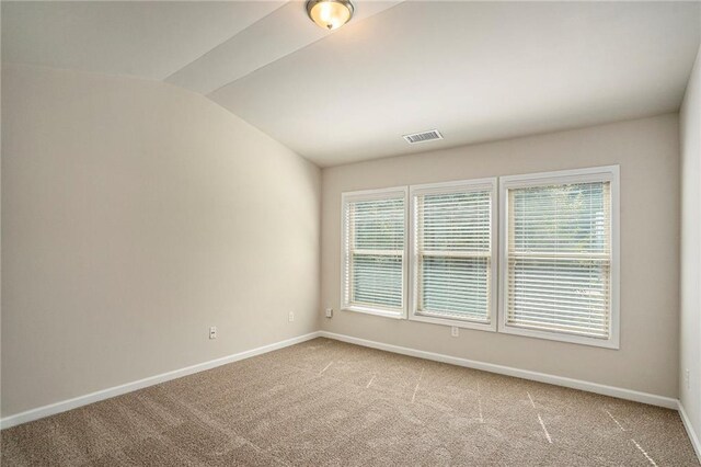 carpeted spare room with lofted ceiling, visible vents, and baseboards