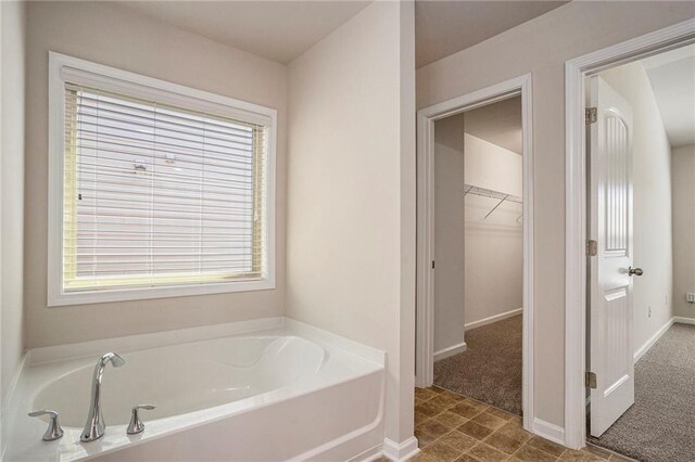 full bathroom featuring baseboards, a walk in closet, and a bath