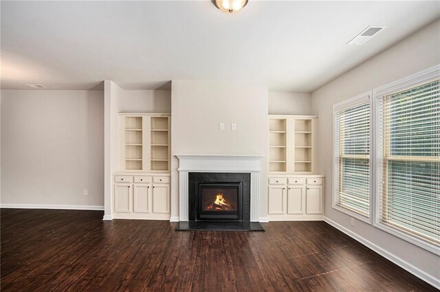 unfurnished living room featuring a warm lit fireplace, baseboards, visible vents, and dark wood-type flooring