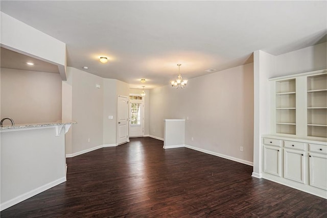 unfurnished living room featuring a chandelier, dark wood-type flooring, and baseboards