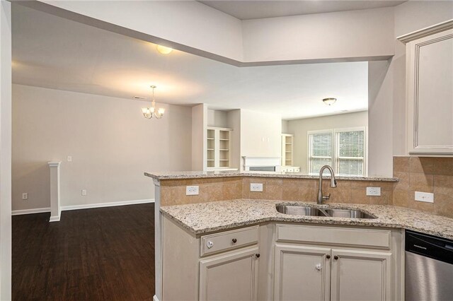 kitchen with light stone counters, backsplash, stainless steel dishwasher, a sink, and a peninsula