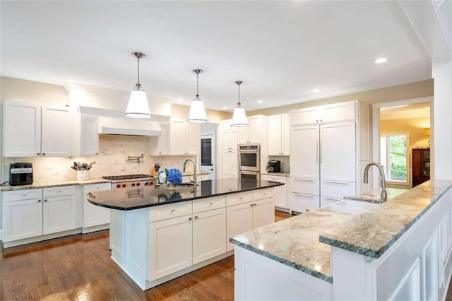 kitchen with decorative backsplash, white cabinets, dark hardwood / wood-style flooring, and an island with sink