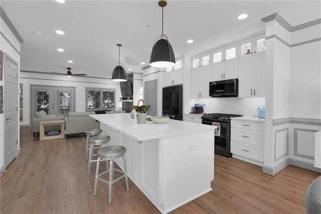 kitchen featuring open floor plan, black appliances, light wood-style flooring, and white cabinetry