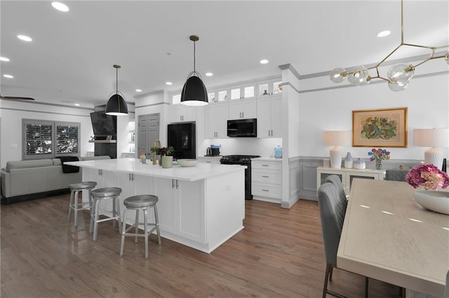 kitchen featuring white cabinets, dark wood finished floors, a kitchen breakfast bar, gas range oven, and black microwave