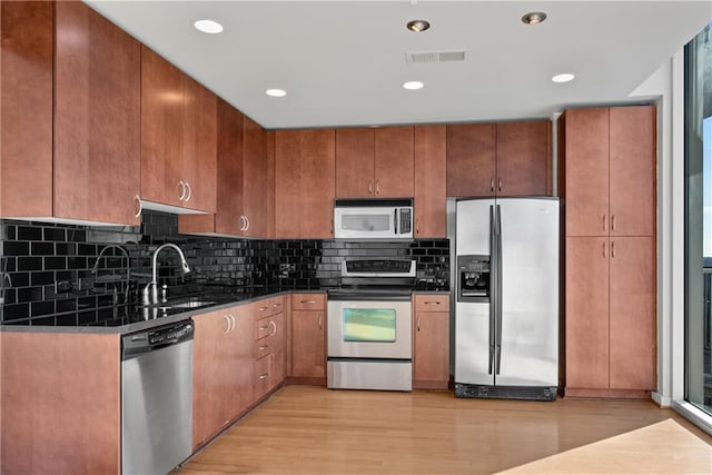 kitchen with sink, light hardwood / wood-style flooring, dark stone countertops, appliances with stainless steel finishes, and backsplash