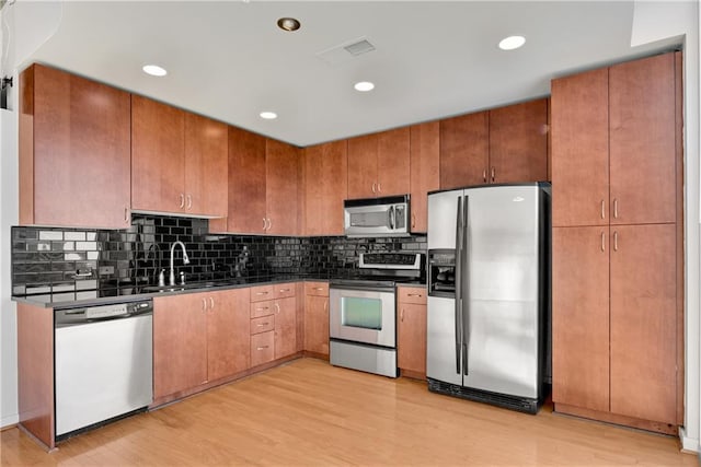 kitchen with appliances with stainless steel finishes, sink, decorative backsplash, and light wood-type flooring