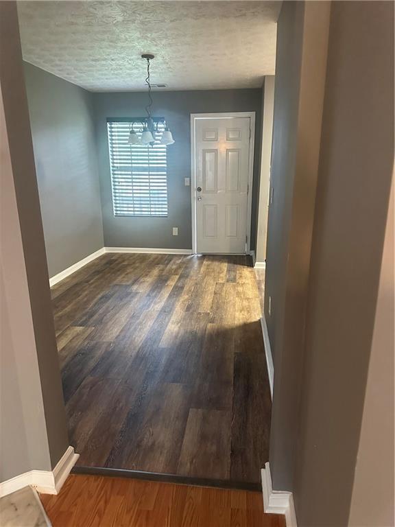 unfurnished dining area with dark hardwood / wood-style flooring, a notable chandelier, and a textured ceiling