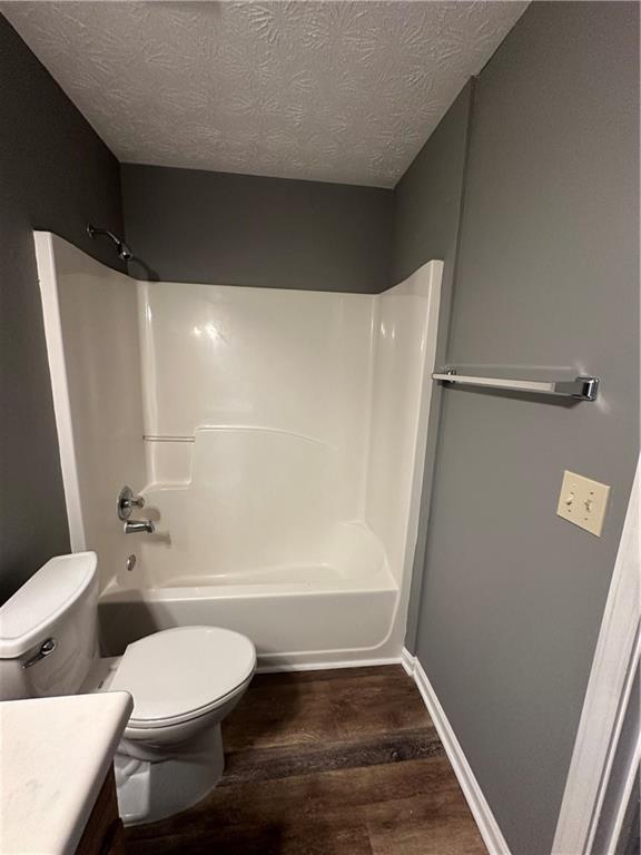 full bathroom with hardwood / wood-style flooring, vanity,  shower combination, toilet, and a textured ceiling