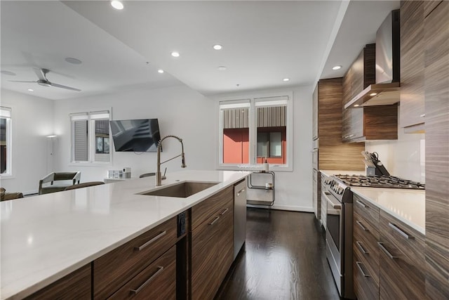 kitchen with appliances with stainless steel finishes, light countertops, wall chimney range hood, and a sink