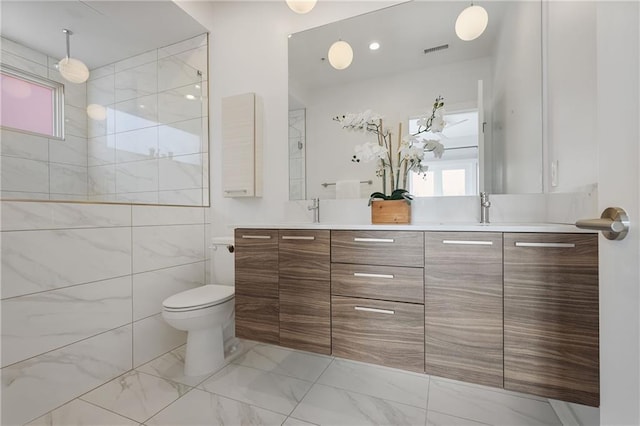 full bath featuring visible vents, toilet, a sink, double vanity, and tiled shower