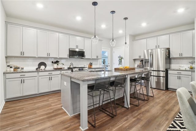 kitchen featuring sink, a kitchen island with sink, hanging light fixtures, stainless steel appliances, and light stone counters