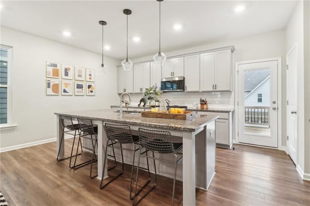 kitchen featuring sink, a breakfast bar area, a kitchen island with sink, hanging light fixtures, and light stone counters