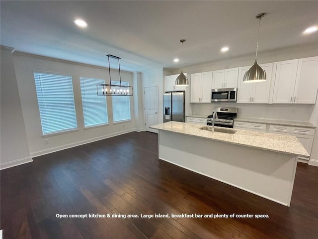 kitchen with light stone counters, hanging light fixtures, a center island with sink, white cabinets, and appliances with stainless steel finishes