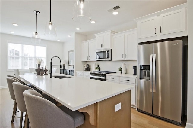 kitchen with a sink, light wood-style floors, a kitchen island with sink, stainless steel appliances, and visible vents