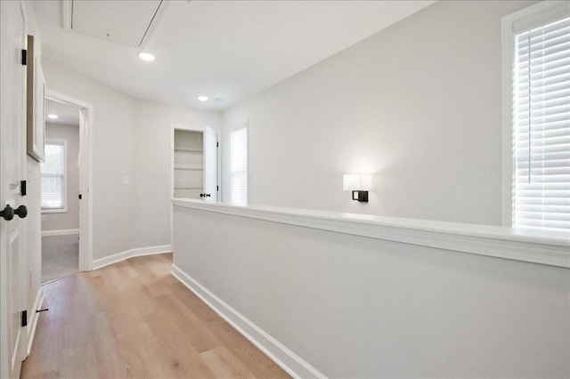hallway featuring baseboards, a healthy amount of sunlight, light wood-style flooring, and attic access