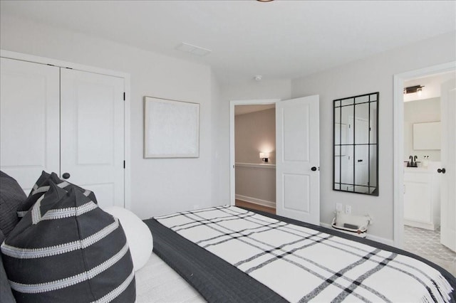 bedroom with a sink, baseboards, a closet, and ensuite bath