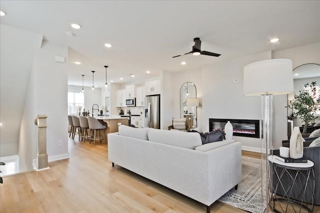 living area with a glass covered fireplace, ceiling fan, recessed lighting, and light wood-style flooring
