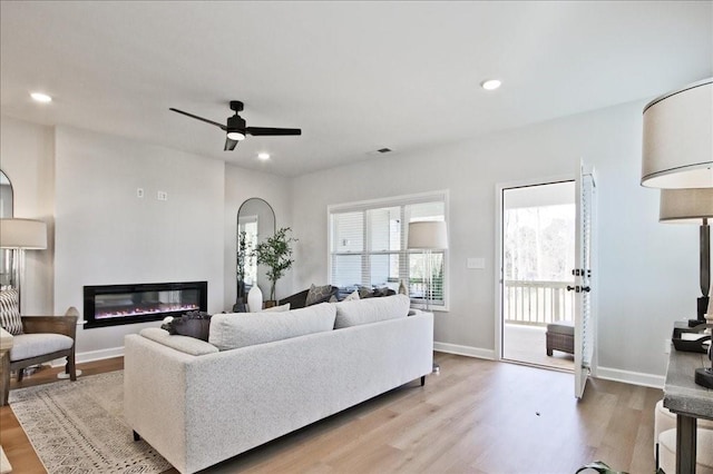 living area with a ceiling fan, a glass covered fireplace, recessed lighting, and light wood-style floors