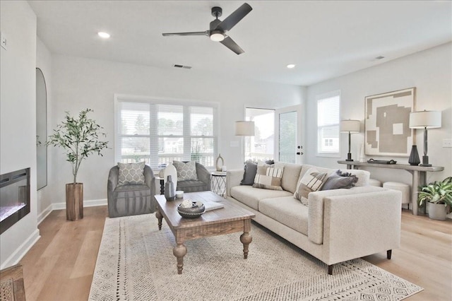 living room featuring a healthy amount of sunlight, a ceiling fan, light wood finished floors, and visible vents