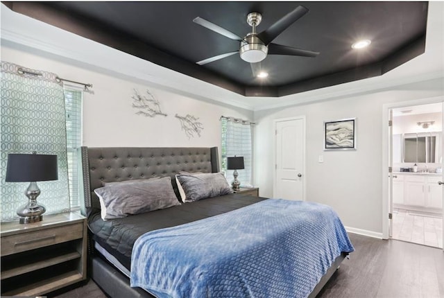 bedroom featuring connected bathroom, a tray ceiling, dark wood-style floors, baseboards, and recessed lighting