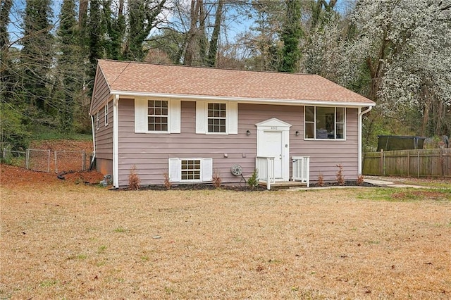 raised ranch featuring a shingled roof, a front yard, and fence