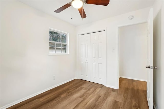 unfurnished bedroom featuring ceiling fan, a closet, baseboards, and wood finished floors