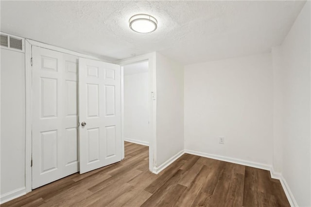 unfurnished bedroom with baseboards, a textured ceiling, visible vents, and wood finished floors