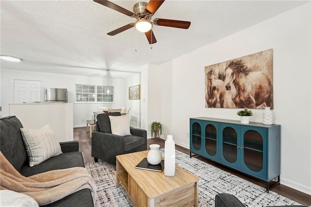 living area featuring ceiling fan, a textured ceiling, baseboards, and wood finished floors