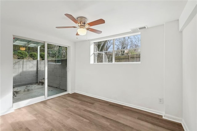 spare room featuring a ceiling fan, wood finished floors, visible vents, and a healthy amount of sunlight