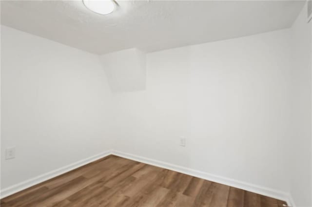 spare room featuring baseboards and dark wood-style flooring