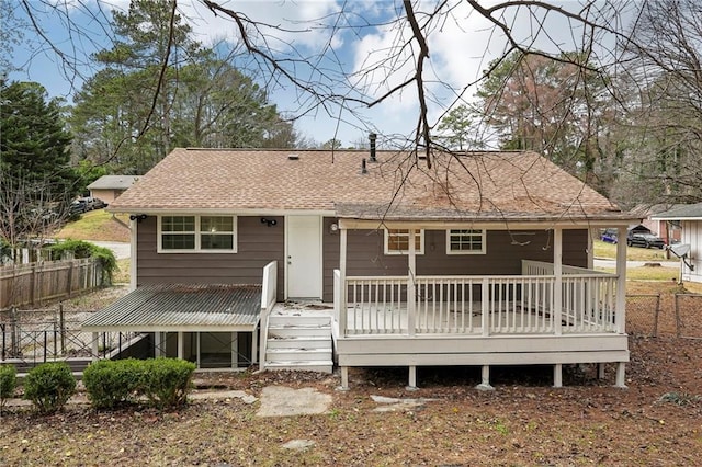 rear view of property with roof with shingles, fence, and a wooden deck